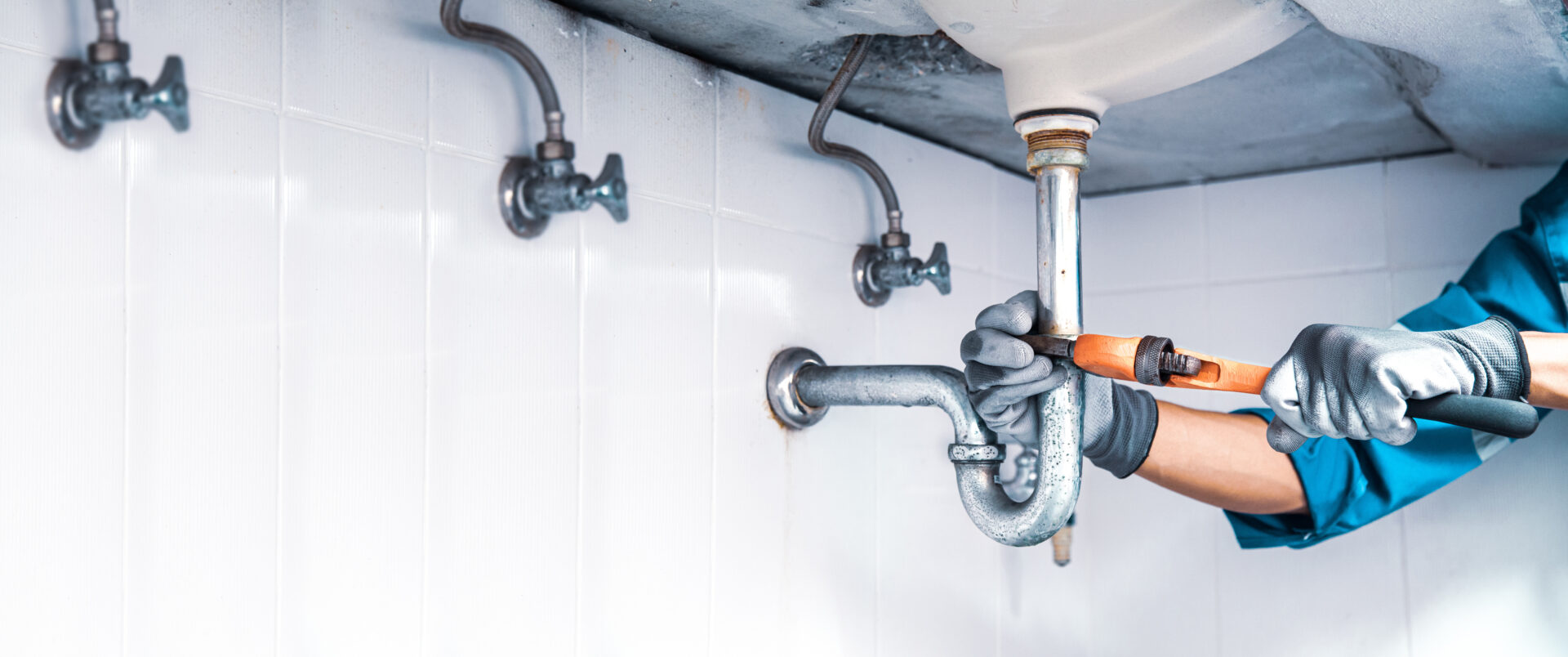 Technician plumber using a wrench to repair a water pipe under the sink