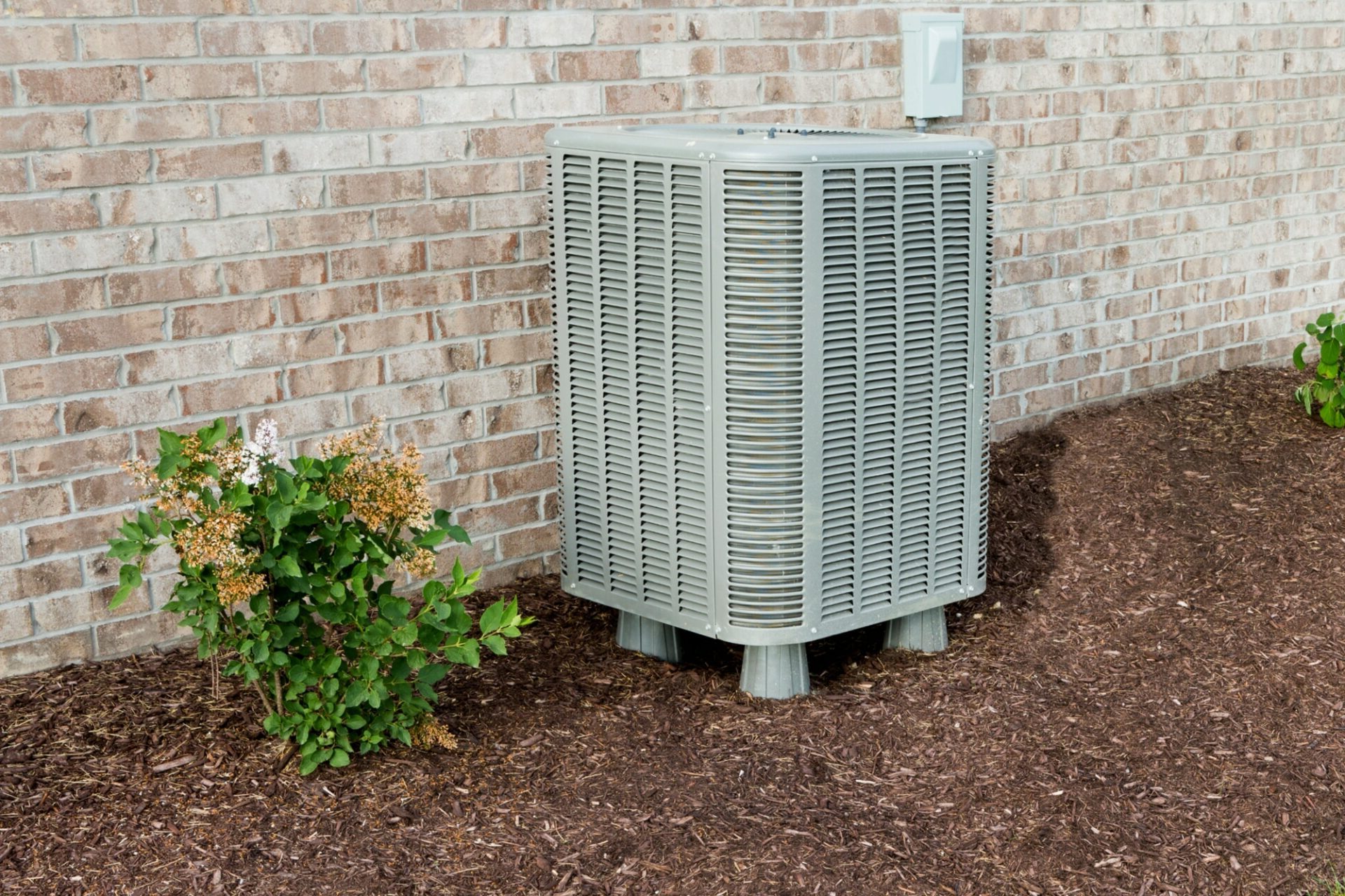 HVAC unit next to a brick home and shrubbery.