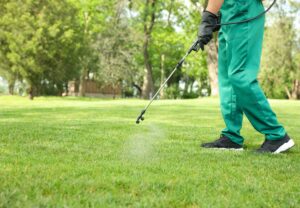 Worker in green exterminator gear spraying pesticide into the grass