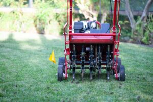 A photo of a red and black lawn aeration machine, sitting on a grass lawn, with a yellow flag next to it