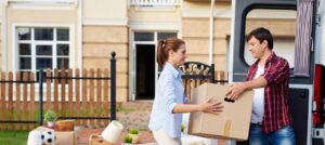 Portrait of man taking cardboard boxes out of moving van in New Mexico and passing them to his wife in front of new house