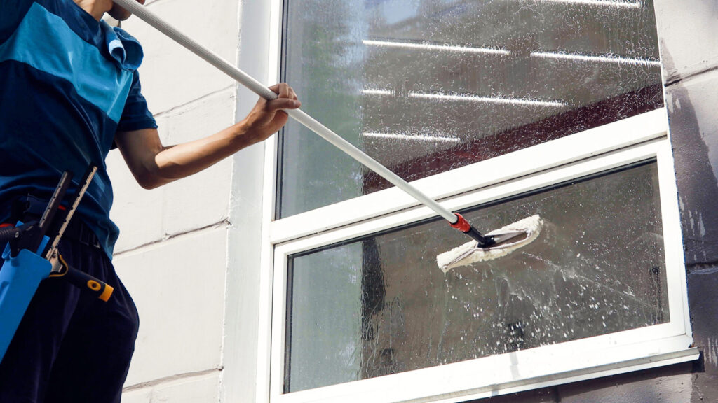 Male professional cleaning service worker cleans the windows on the outside of a house
