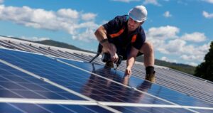 Solar panel technician with drill installing solar panels on roof on a sunny day