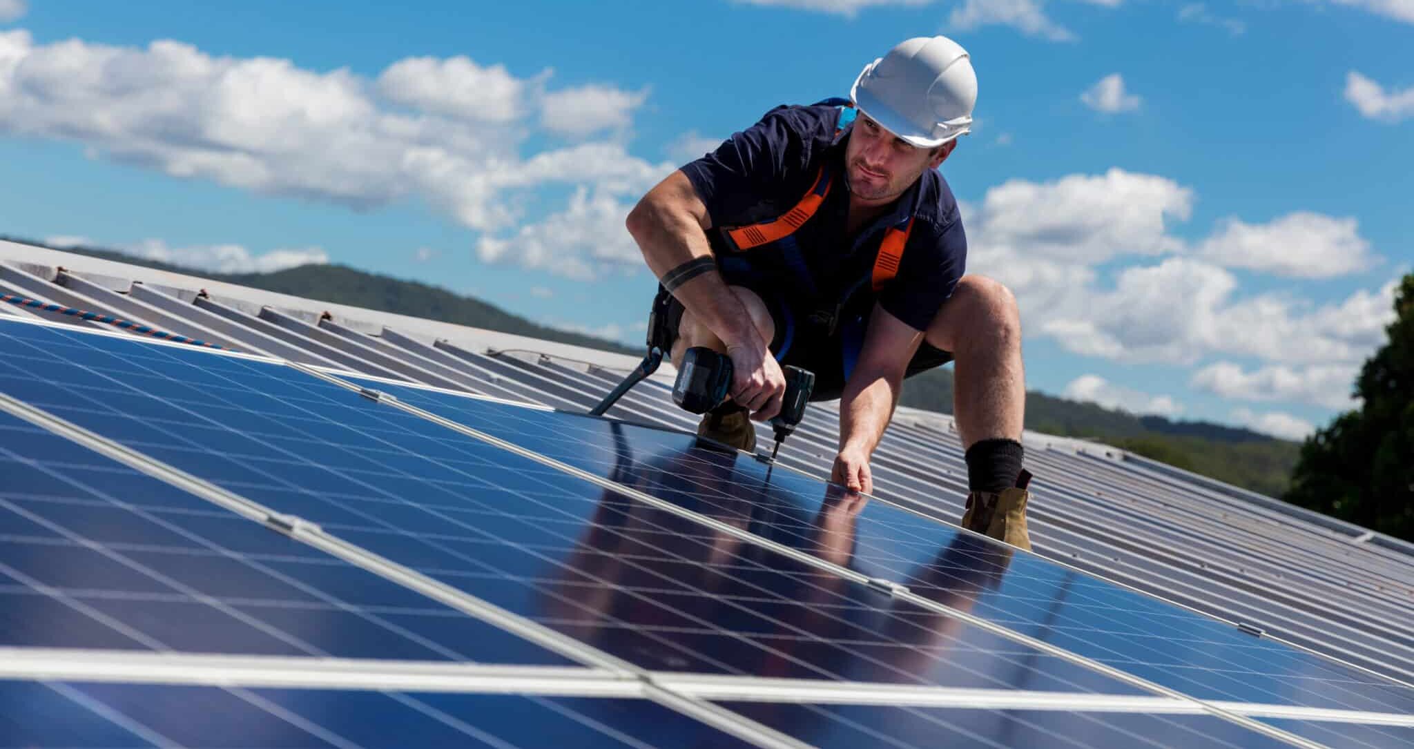 Solar panel technician with drill installing solar panels on roof on a sunny day