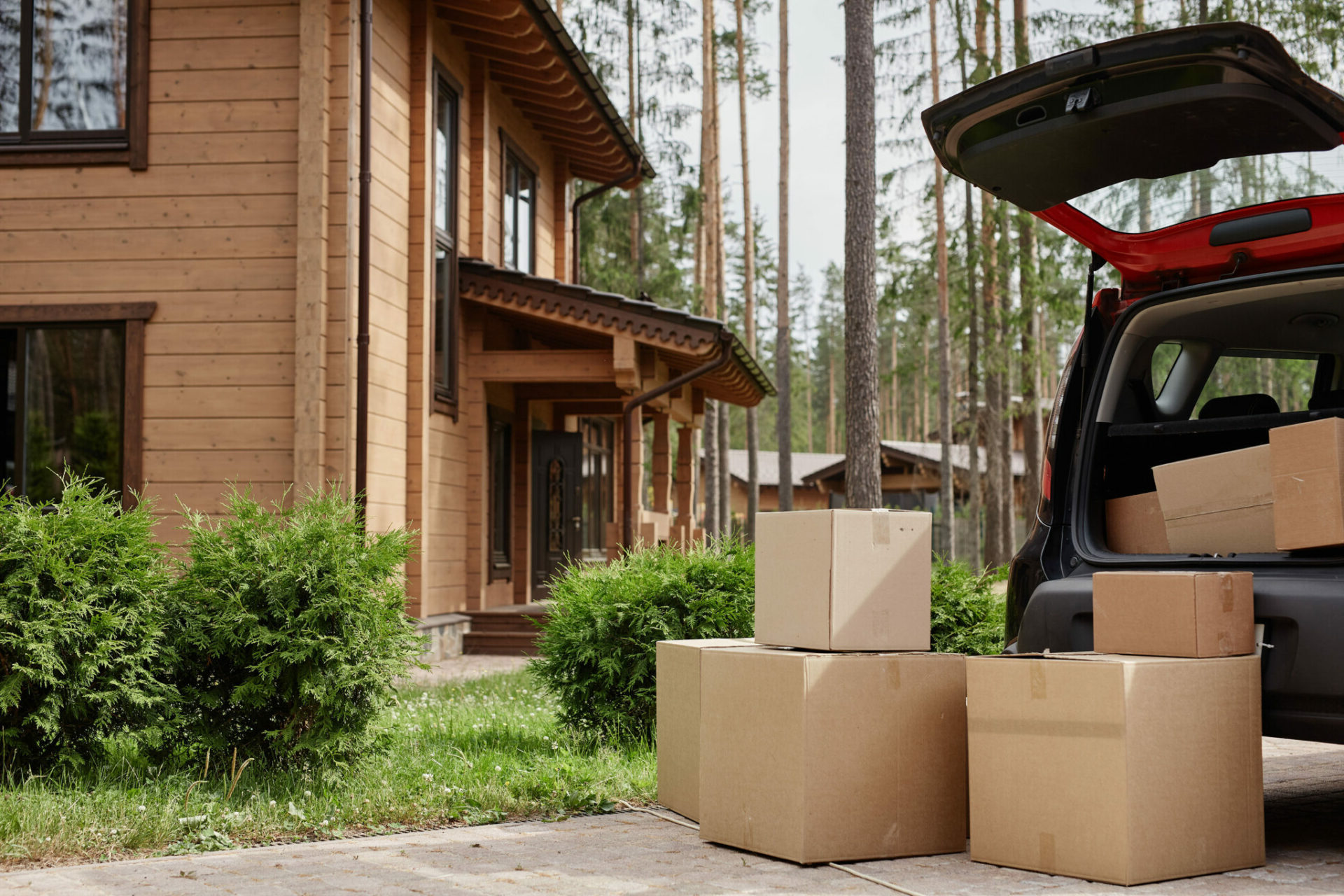 modern wooden house in woods with car and cardboard moving boxes in foreground