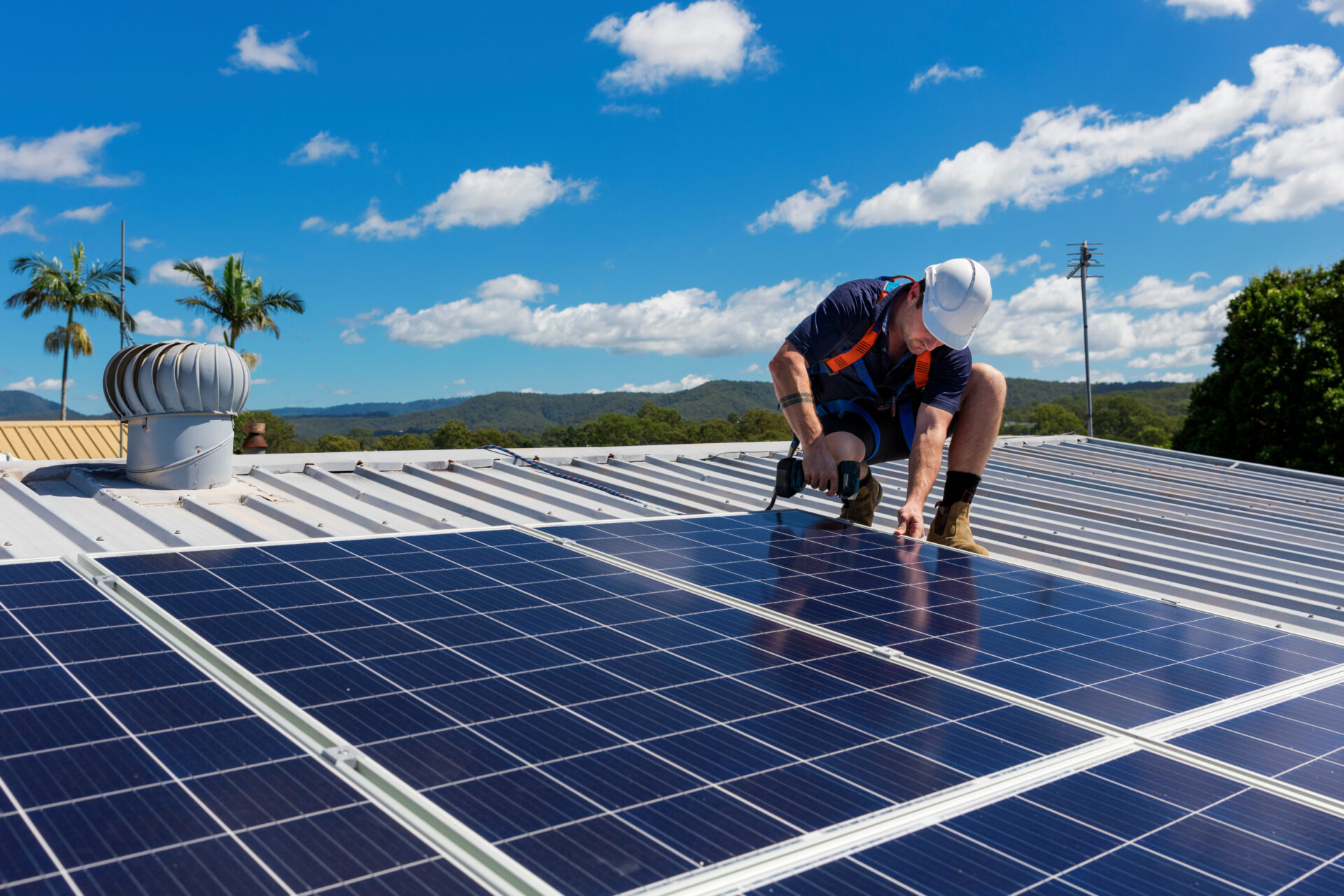 Solar panel technician with drill installing solar panels on roof on a sunny day