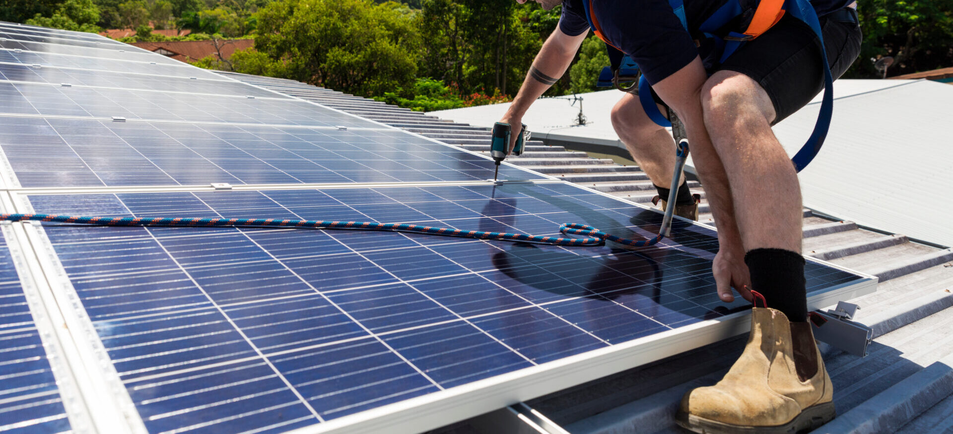 Solar panel technician with drill installing solar panels on roof on a sunny day