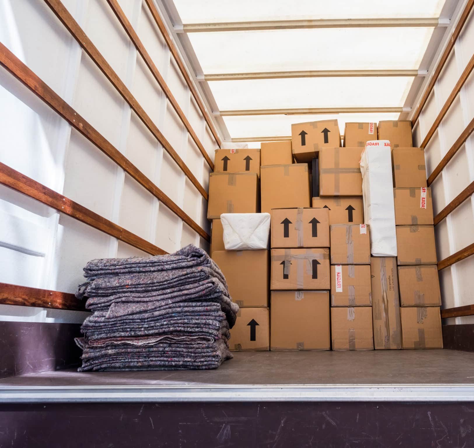The inside of a UHaul van, showing fabric blankets stacked and a background of cardboard boxes.