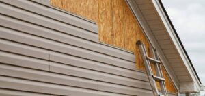 New beige vinyl siding being installed over an osb (oriented strand board) substrate on a residential house in the Southeastern USA region on a cloudy day. The old vinyl siding was being replaced after a hail storm.