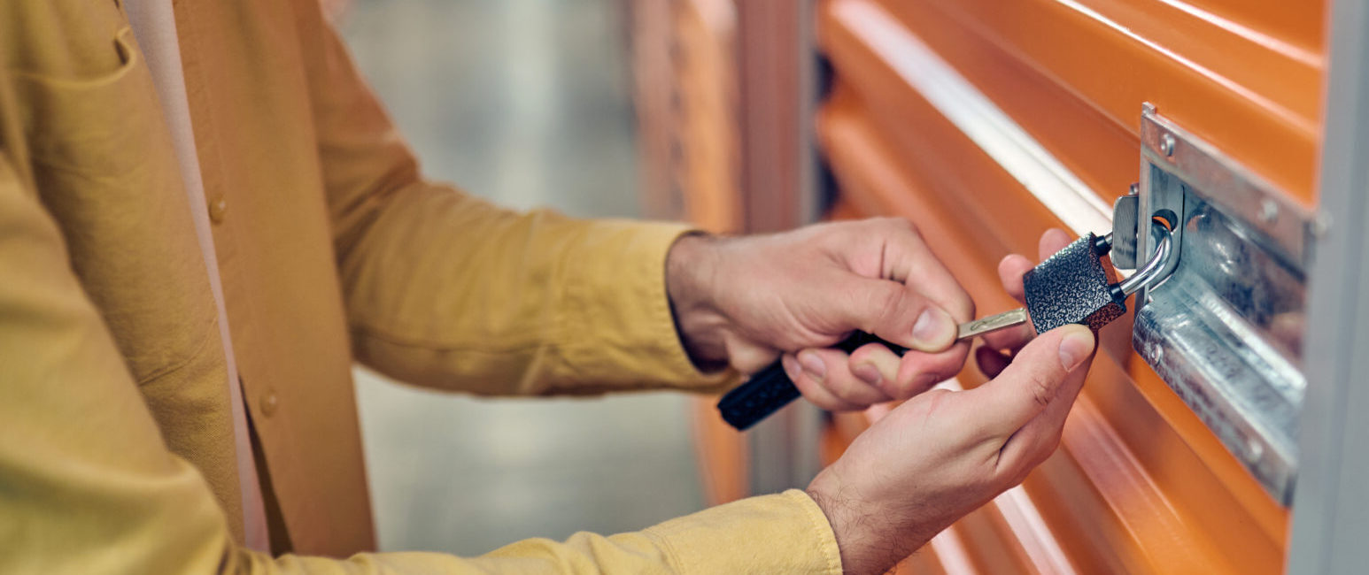 Cropped photo of an authorized warehouse employee putting a metal key into the padlock hole