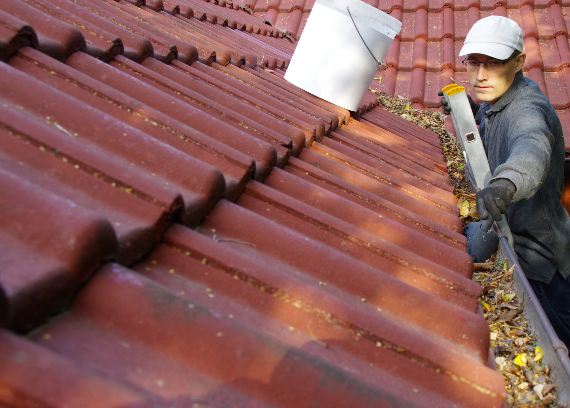 A man on a ladder cleans a gutter full of leaves