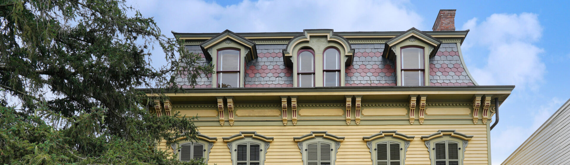 Ornate 19th century American house with full width porch on a sunny day. The house has a mansard roof