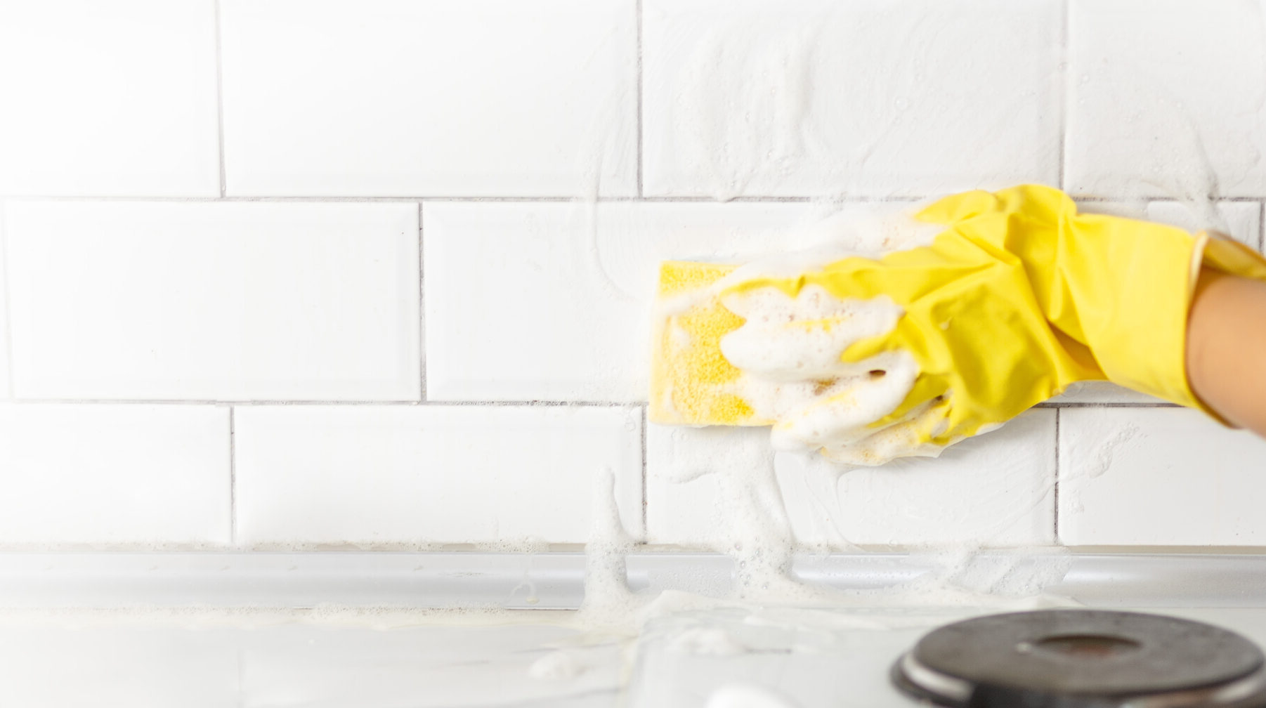 Hand and glove cleaning white kitchen tiles.