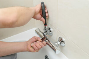 Person with wrench fixing leaky bathtub faucet.