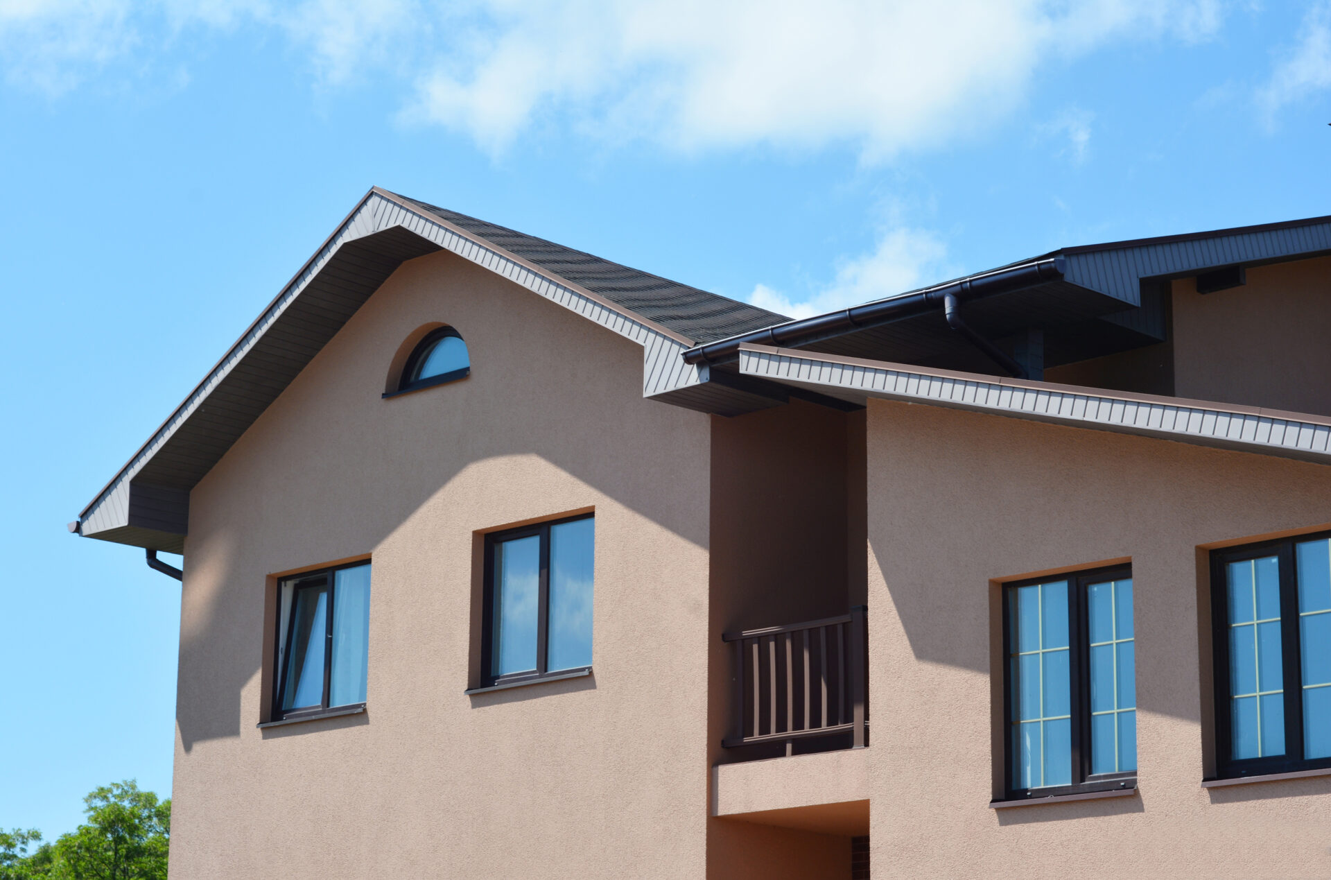Modern house with asphalt shingles roof, balcony, rain gutter pipeline and soffit boards outdoors.
