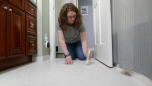 Woman cleaning grout on the bathroom floor.