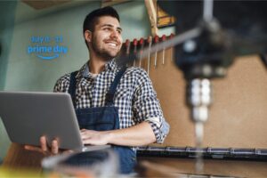 Man in overalls standing in workshop smiling holding a laptop