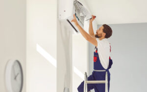 Professional technician standing on a ladder in the room repairing or installing air conditioner.