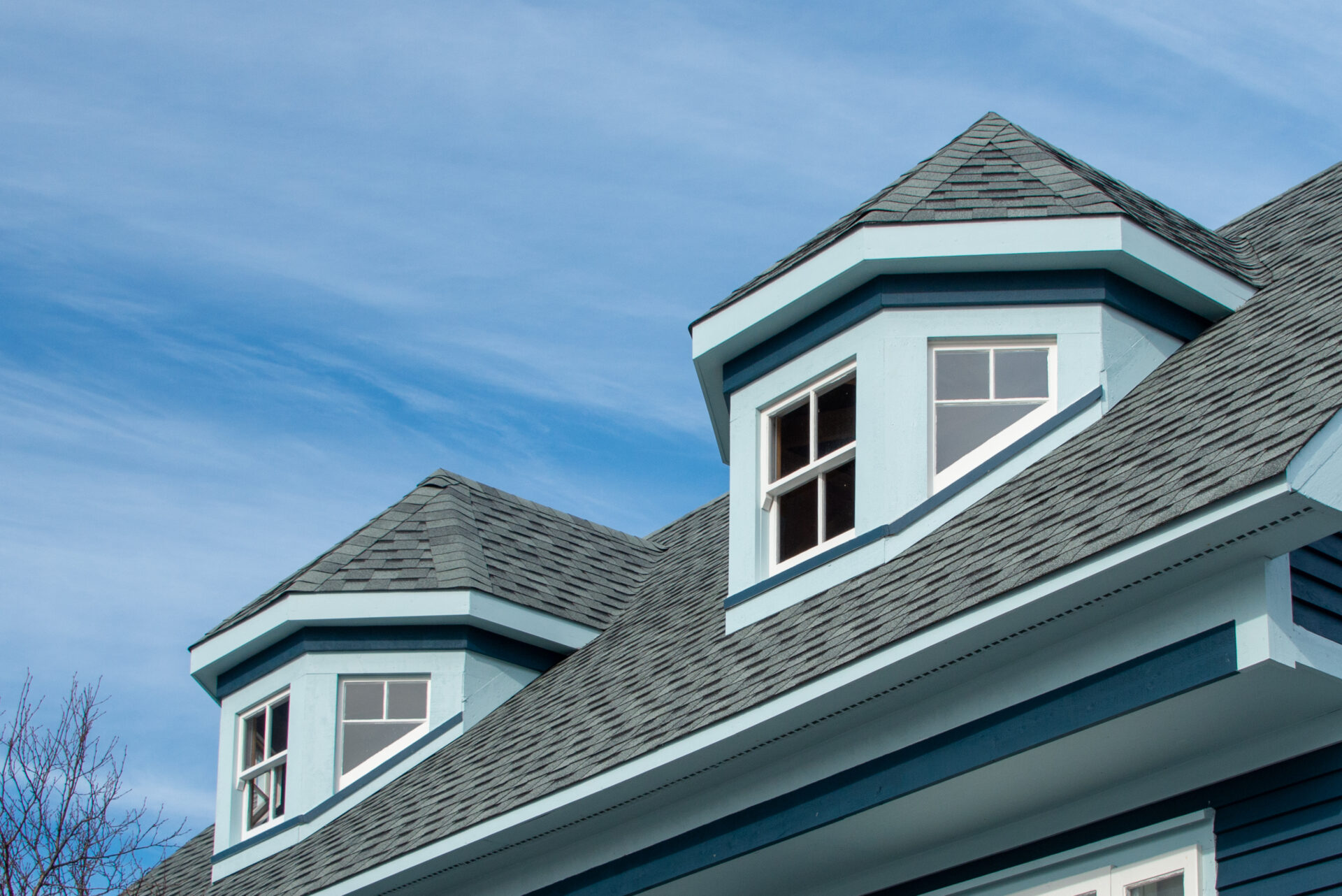 The exterior view of two polygonal dormers on a modern blue rooftop of a wooden house.