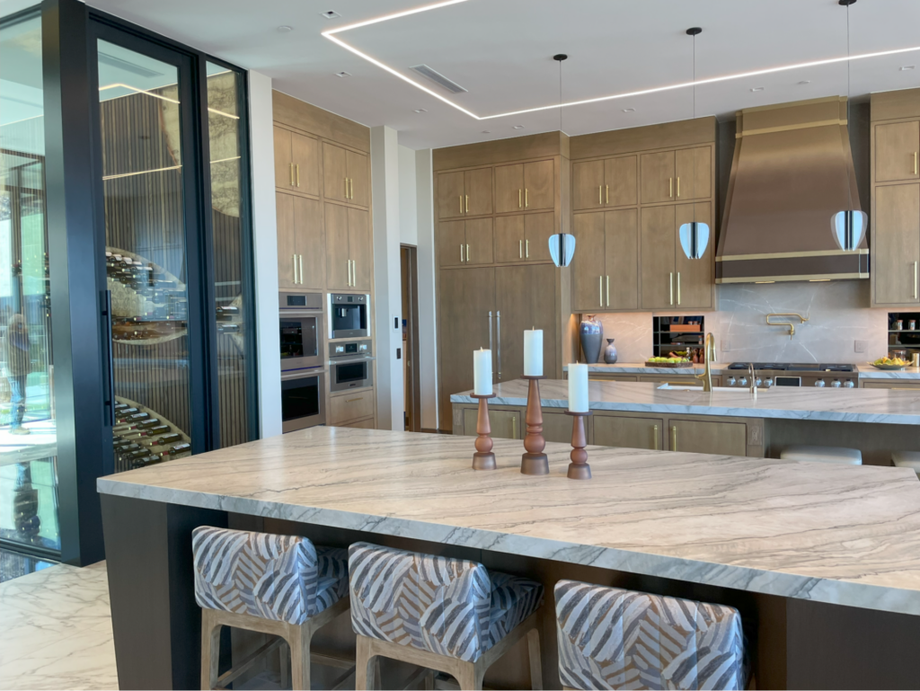 The kitchen in the “New American Home” at the 2025 International Builders Show featured bold, spacious islands with granite countertops, earth-toned cabinets, and brass fixtures.