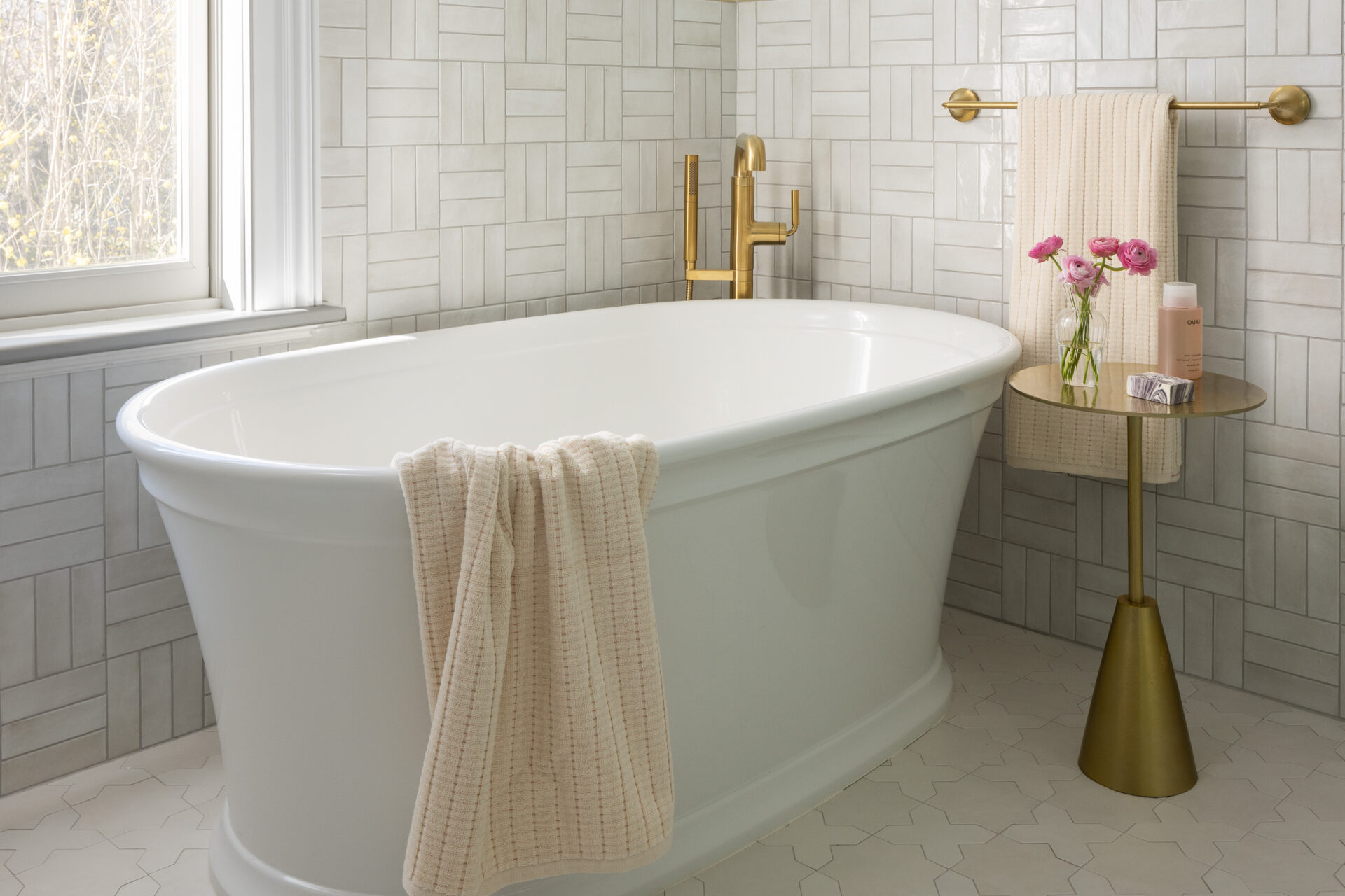 Elegant bathroom with a white freestanding tub, gold fixtures, and a small round table.