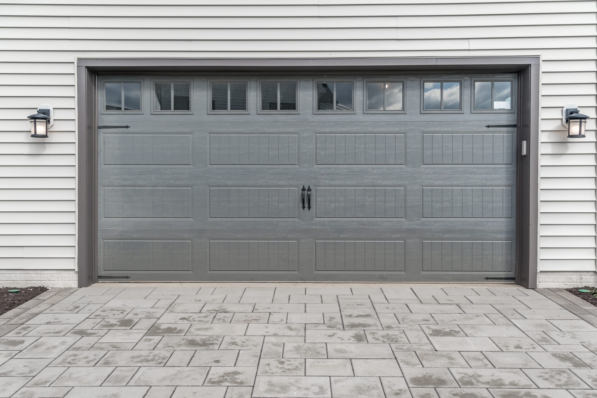 Gray two single car garage door framed with architectural stone to add accent, with transom light windows divided by muntins grills.