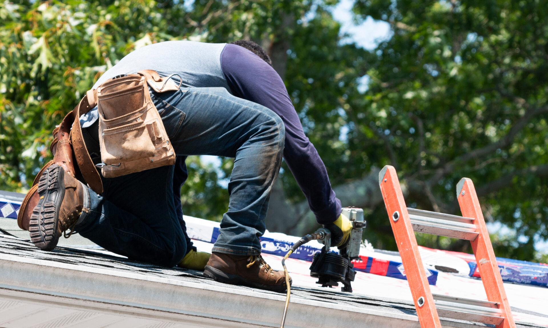 Contractor using nail gun replacing roof shingles on a roof.