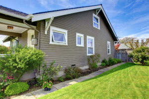 View of the clapboard siding house socle with white windows and green lawn.