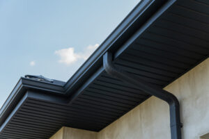 Close view of a roof edge and downspout against a bright blue sky.