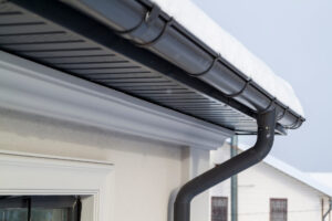 Corner of the house with new gray metal tile roof and rain gutter at winter.